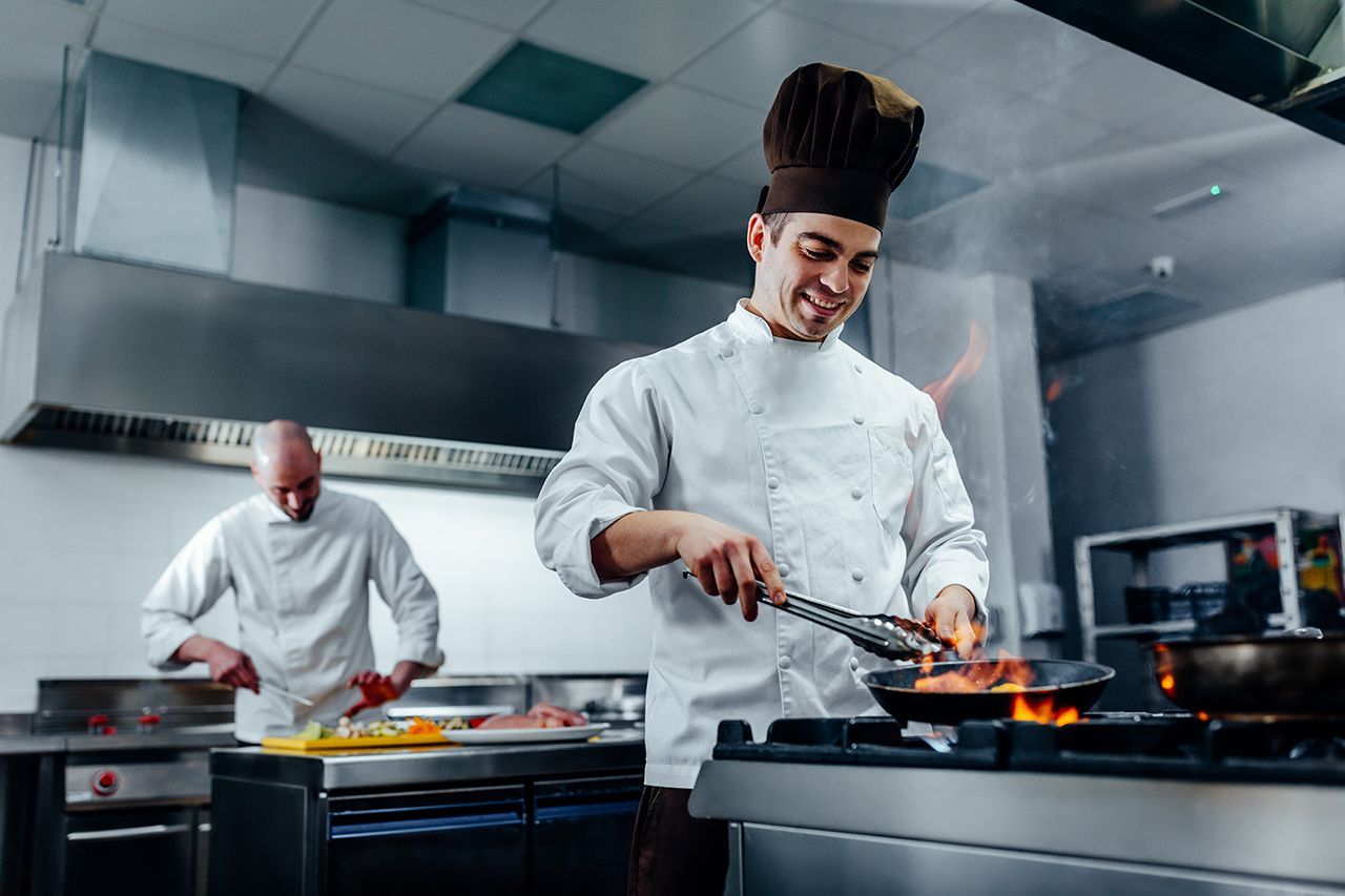 two chefs are cooking food in a commercial kitchen