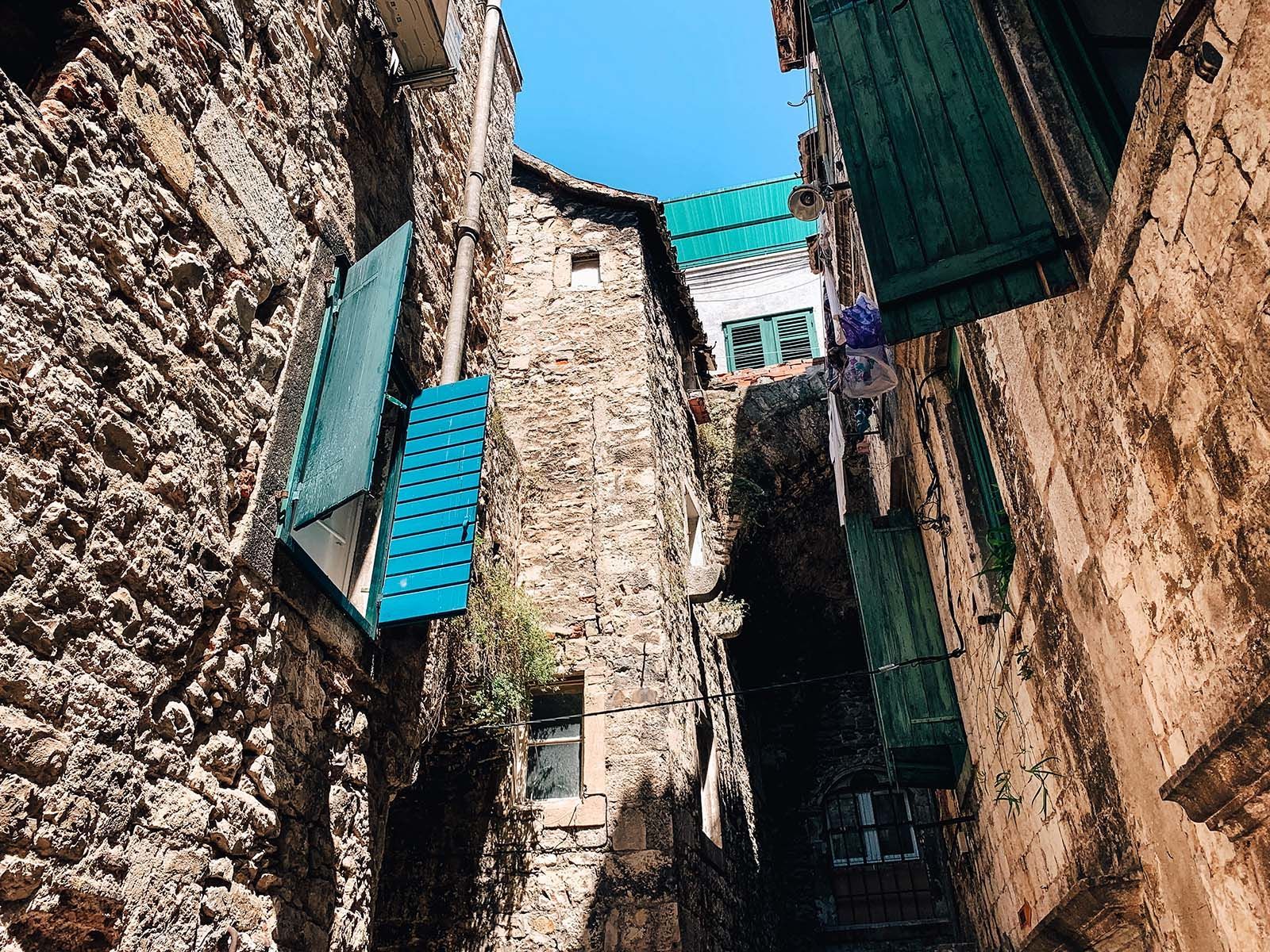 a narrow alleyway between two stone buildings with green shutters on the windows