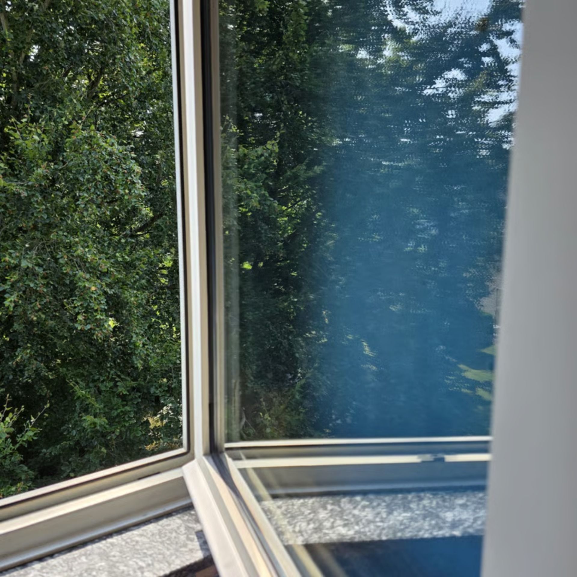 Fensterecke mit Bäumen im Freien. Blauer Dunst auf dem Glas; leuchtend grünes Laub im Hintergrund.