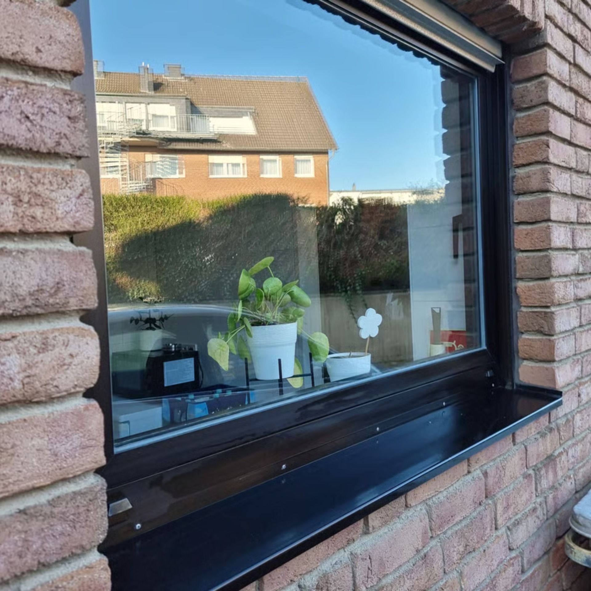 Fenster mit schwarzem Rahmen und Blumenkasten, das ein Backsteingebäude und die Nachbarschaft widerspiegelt.