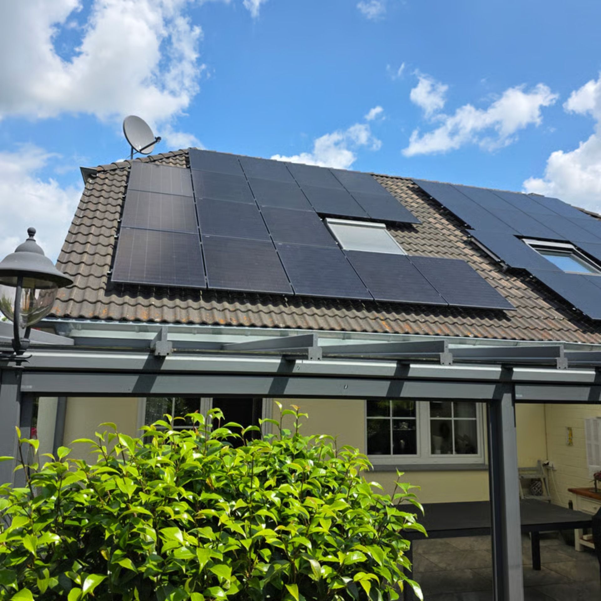 Solarmodule auf einem Ziegeldach bei klarem Himmel, eine Antenne und eine Außenterrasse mit Pflanzen.