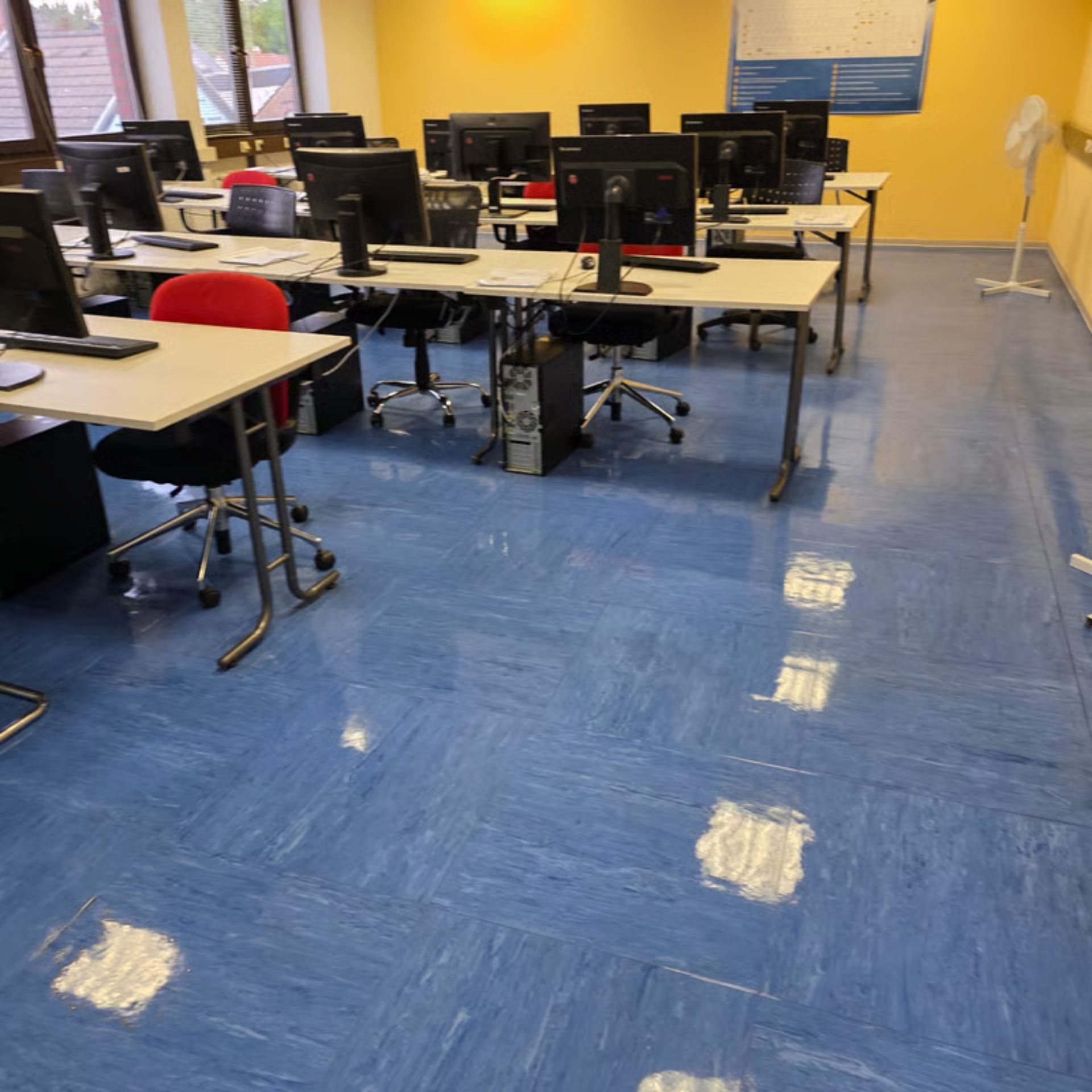 Computerlabor mit blauem Boden, Reihen von Schreibtischen mit Computern und roten und schwarzen Stühlen.