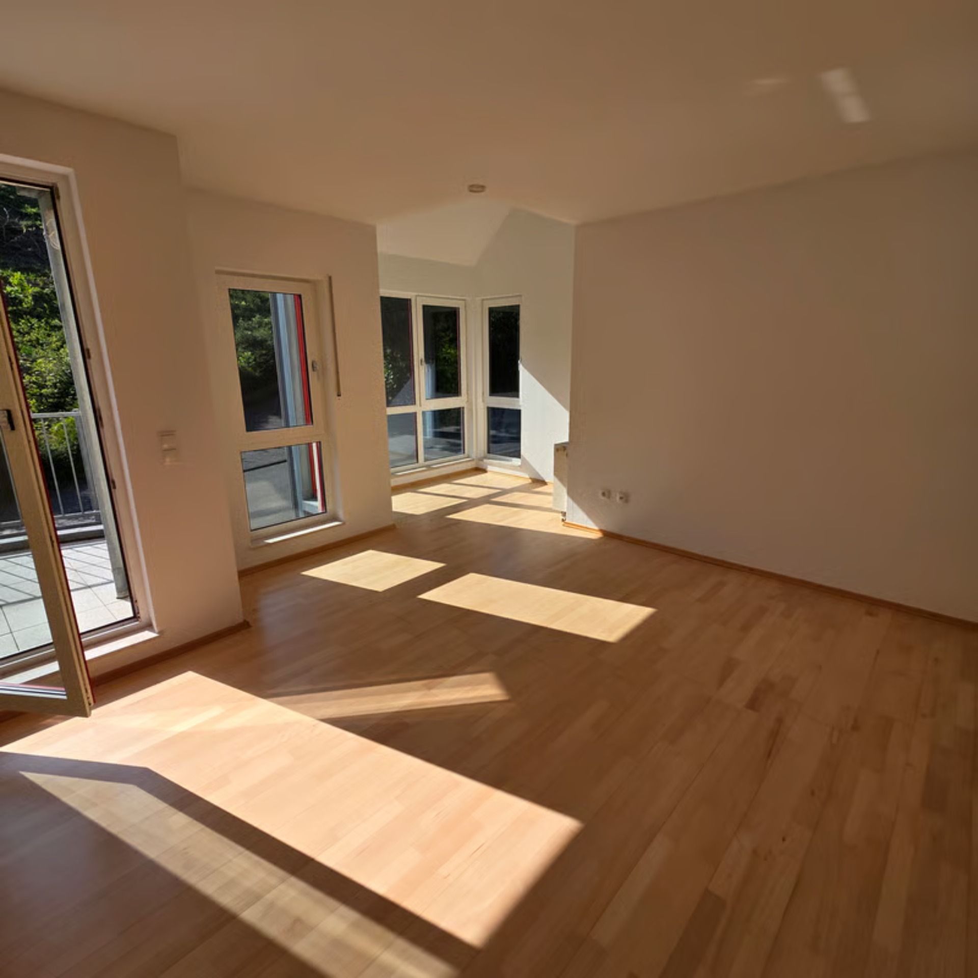 Leerer Raum mit Holzboden, Fenstern und hellem Sonnenlicht.