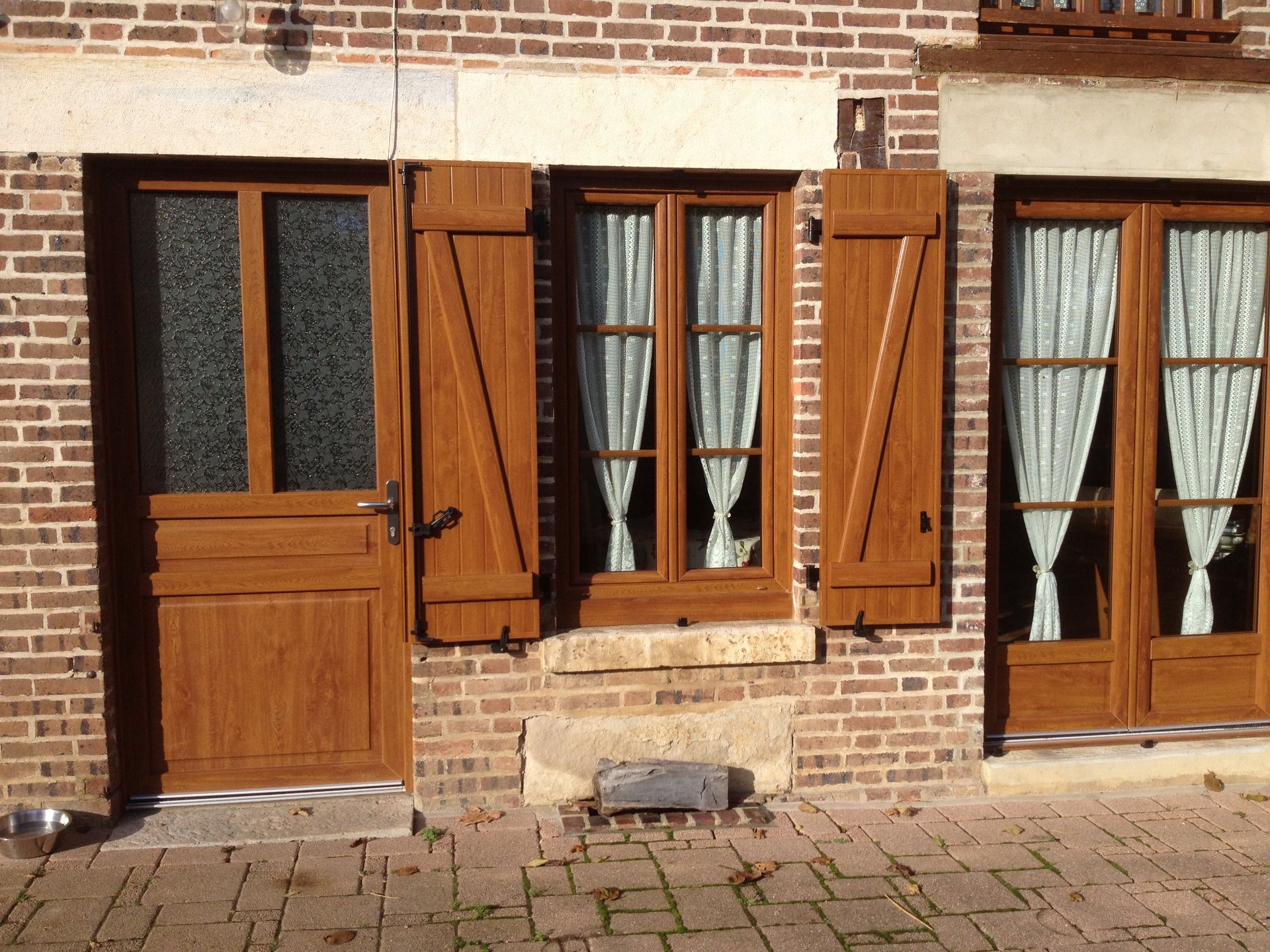 Façade d'une maison en briques avec une porte d'entrée, une fenêtre et une porte-fenêtre en bois.