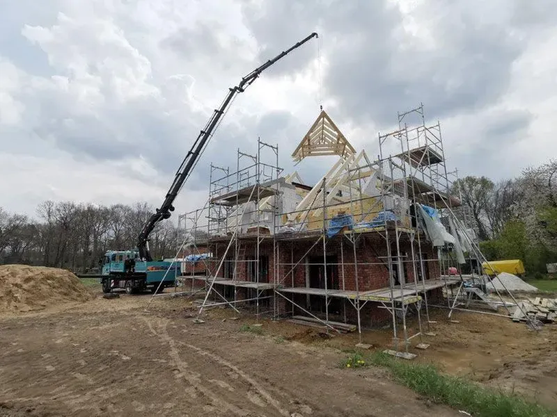 Ein Kran hebt eine Holzkonstruktion auf ein im Bau befindliches Gebäude.