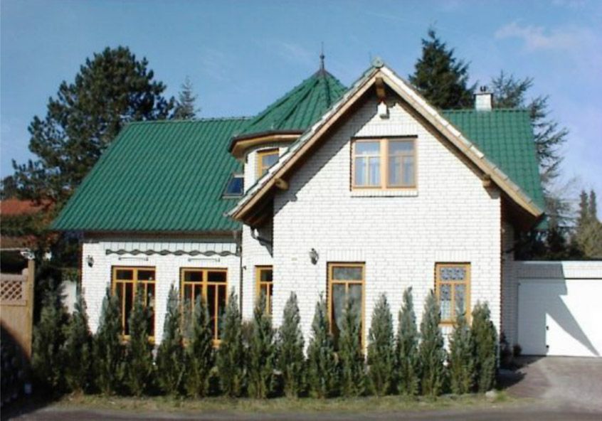 Ein weißes Haus mit einem grünen Dach ist von Bäumen umgeben