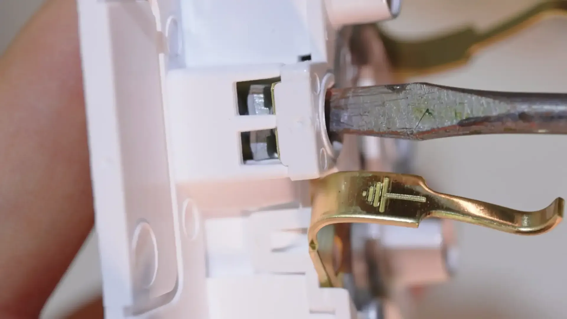 Primer plano de una toma de corriente blanca con un destornillador insertando un cable.
