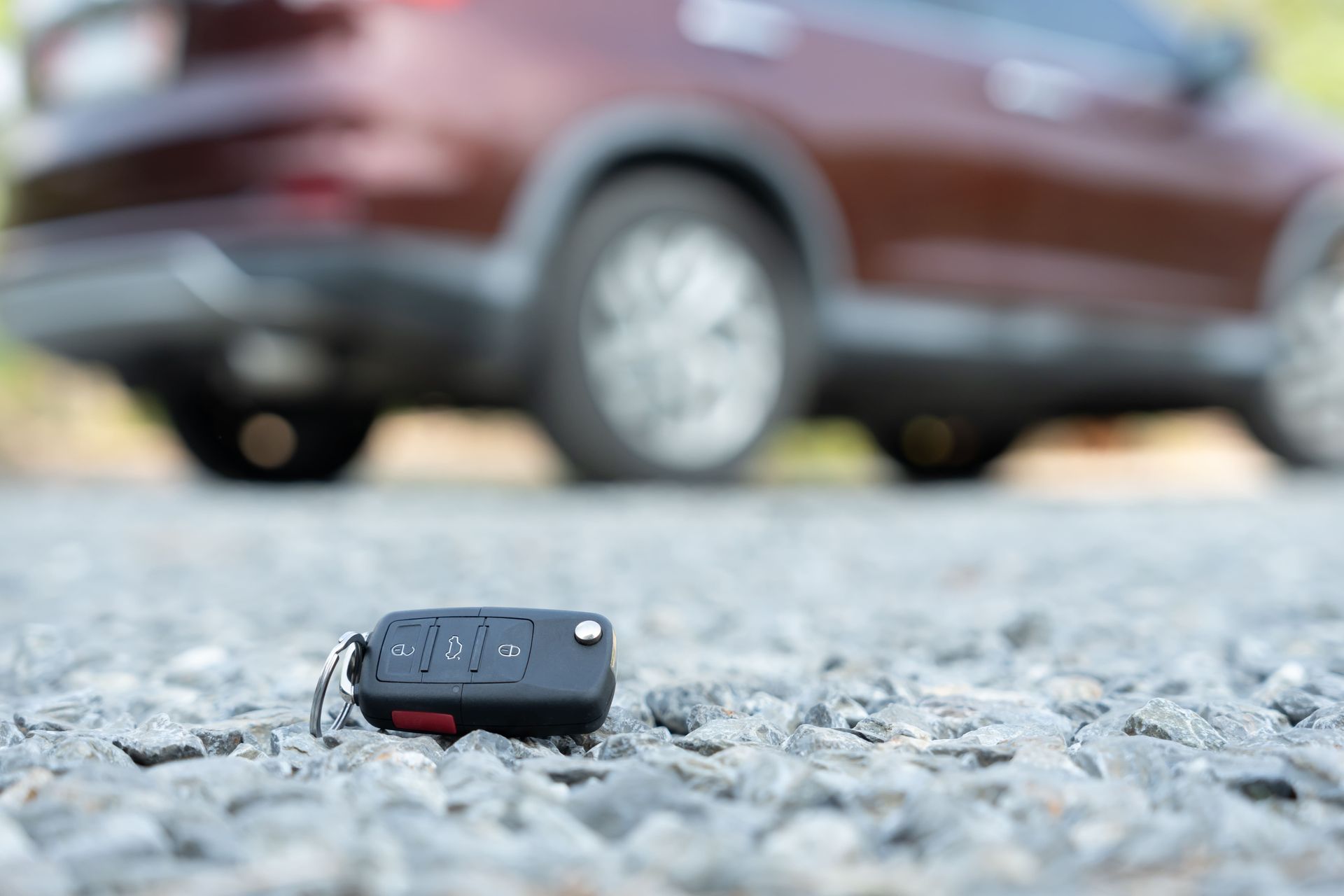Llave de coche sobre la grava delante de un coche granate.