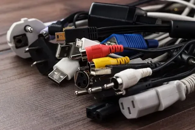 Montón de cables y enchufes electrónicos variados sobre una superficie de madera.