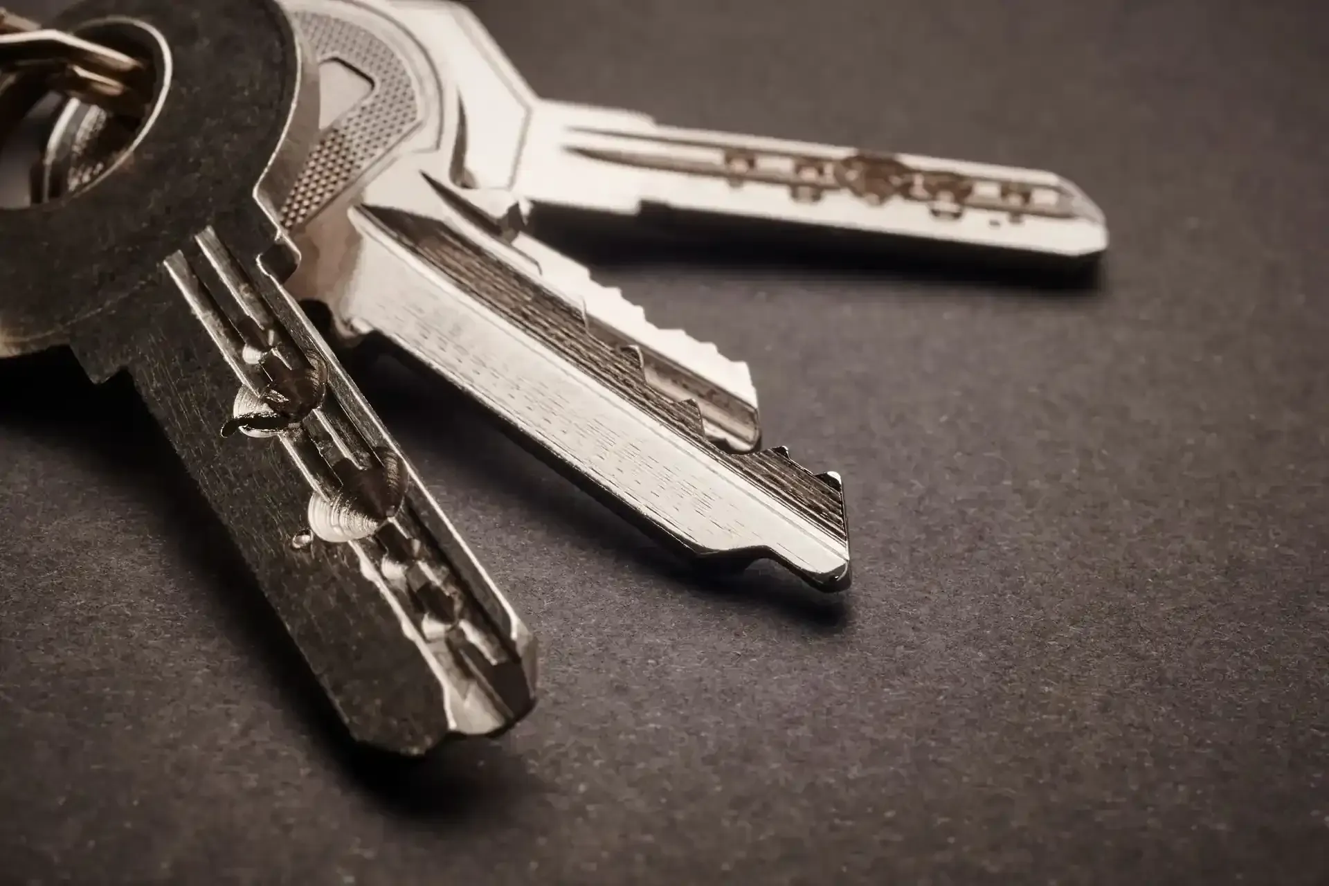 Primer plano de tres llaves plateadas sobre una superficie oscura.