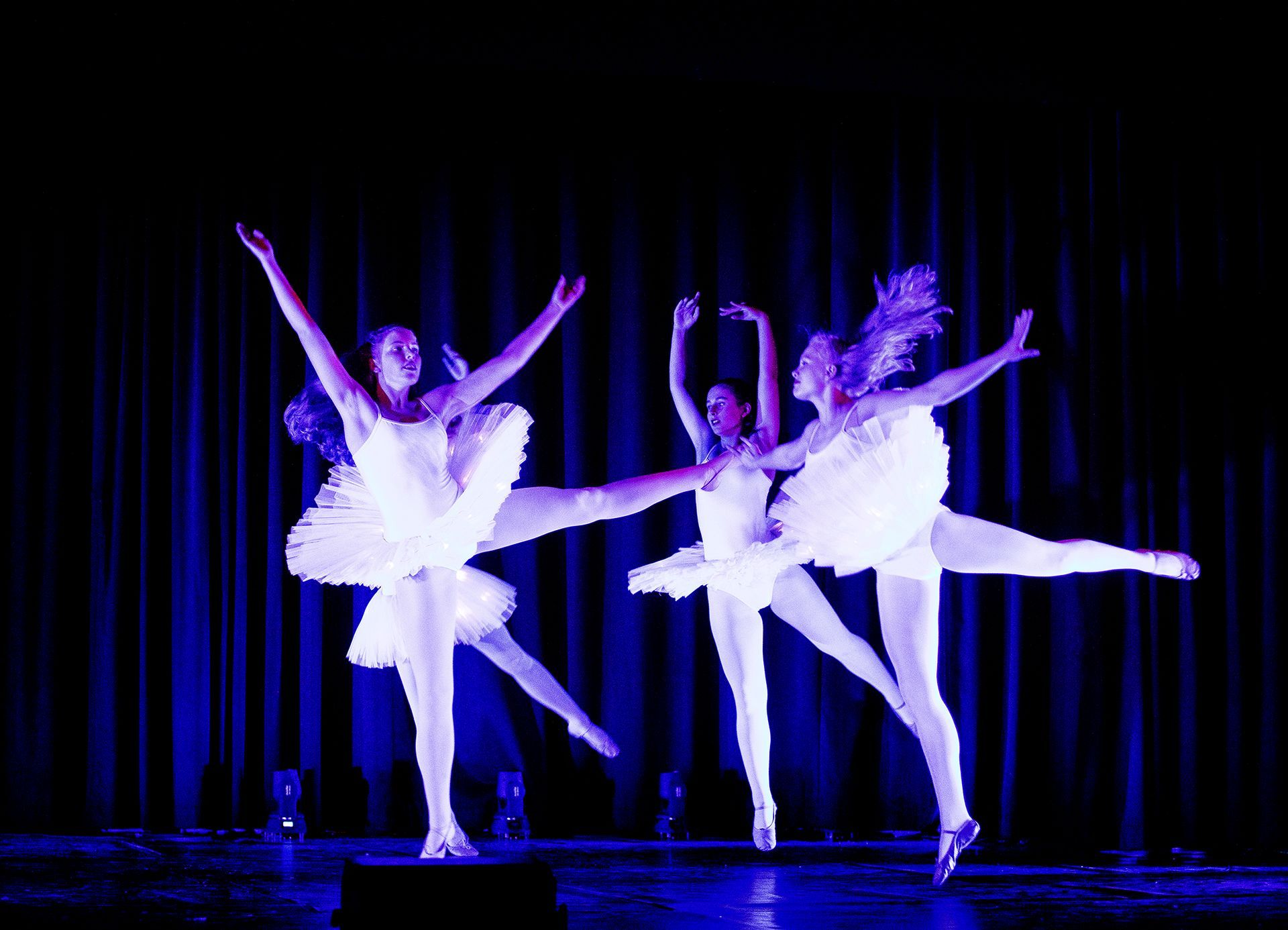 Eine Gruppe Ballerinas tanzt auf einer Bühne vor einem blauen Vorhang.