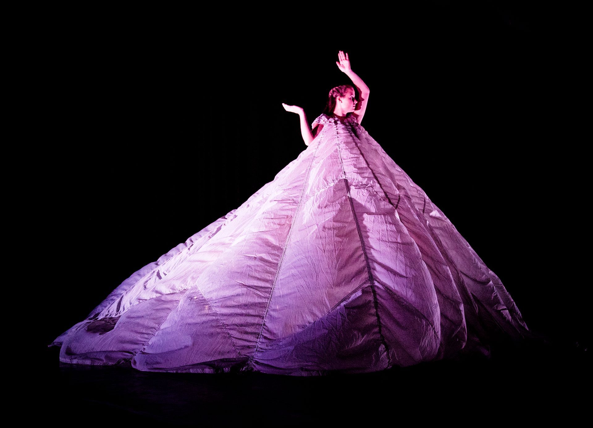 Eine Frau in einem langen lila Kleid tanzt auf einer Bühne.