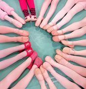 Ein Kreis aus den Beinen von Balletttänzerinnen in rosa Strumpfhosen und Spitzen- oder Ballettschuhen auf einem grünen Boden.