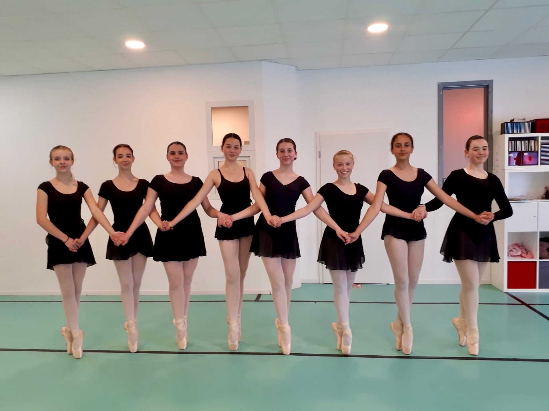 Eine Gruppe junger Ballerinas posiert in einem Tanzstudio für ein Foto.