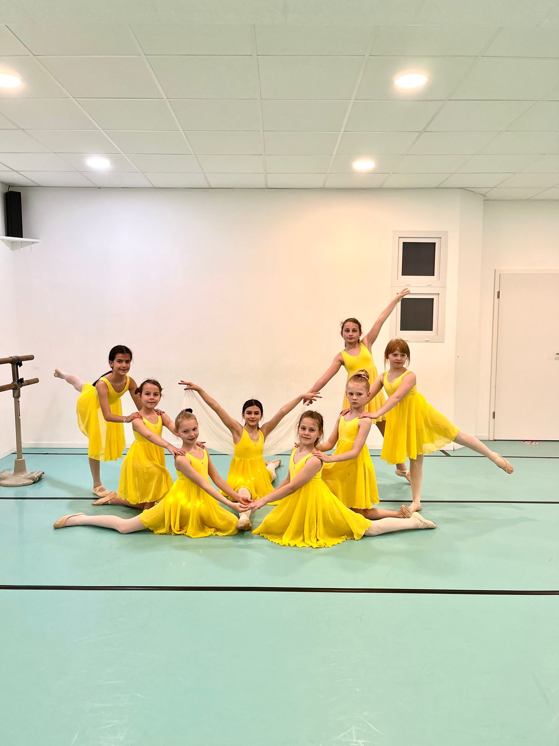 Eine Gruppe junger Mädchen in gelben Kleidern posiert in einem Tanzstudio für ein Foto.
