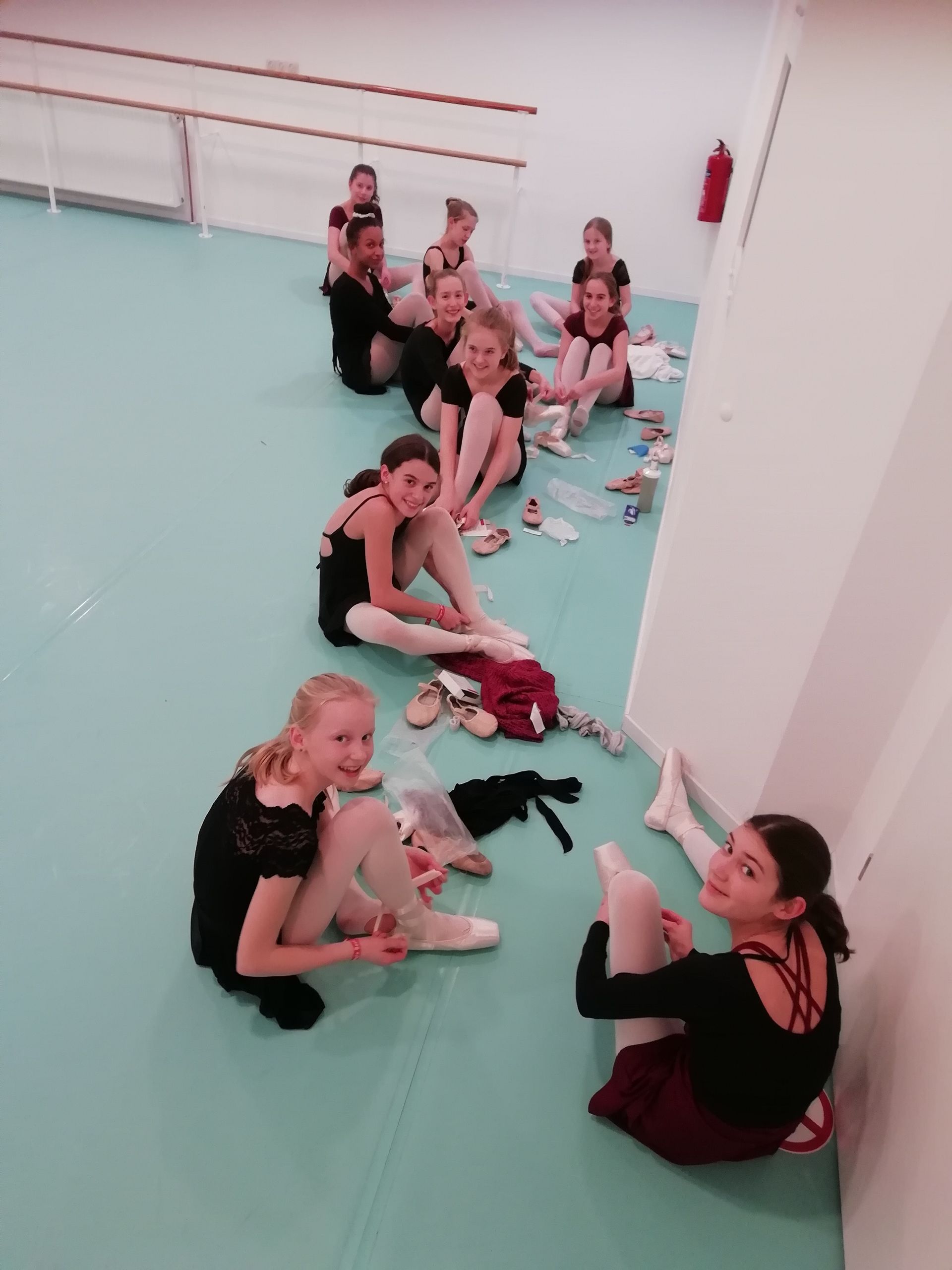 Eine Gruppe junger Mädchen sitzt in einem Tanzstudio auf dem Bode.