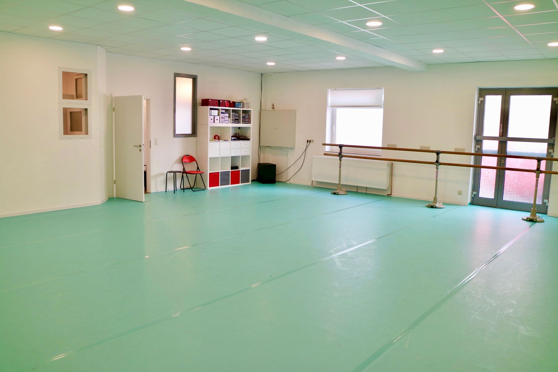 Ein großes leeres Tanzstudio mit grünem Boden und einem Spiegel.