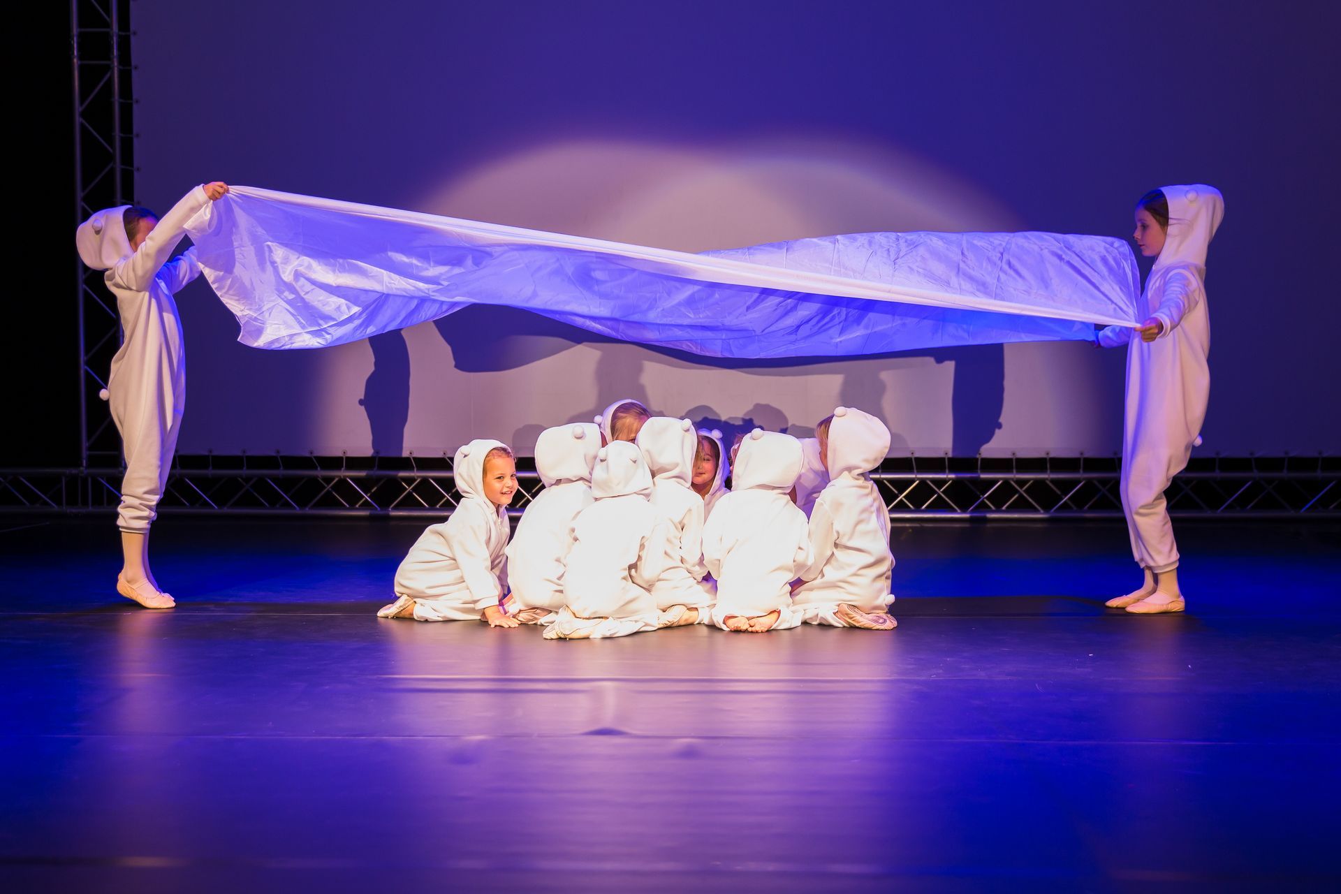 Eine Gruppe Kinder hält auf einer Bühne ein großes weißes Tuch.