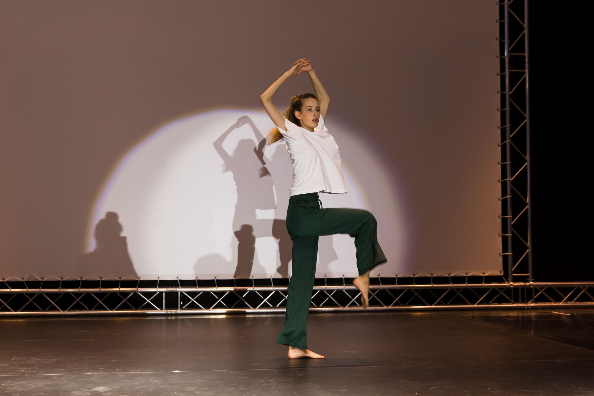 Eine Frau in einem weißen Hemd und grünen Hosen tanzt auf einer Bühne.