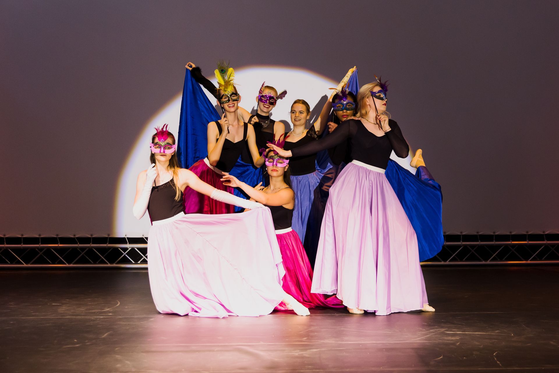 Eine Gruppe maskierter Frauen tanzt auf einer Bühne.