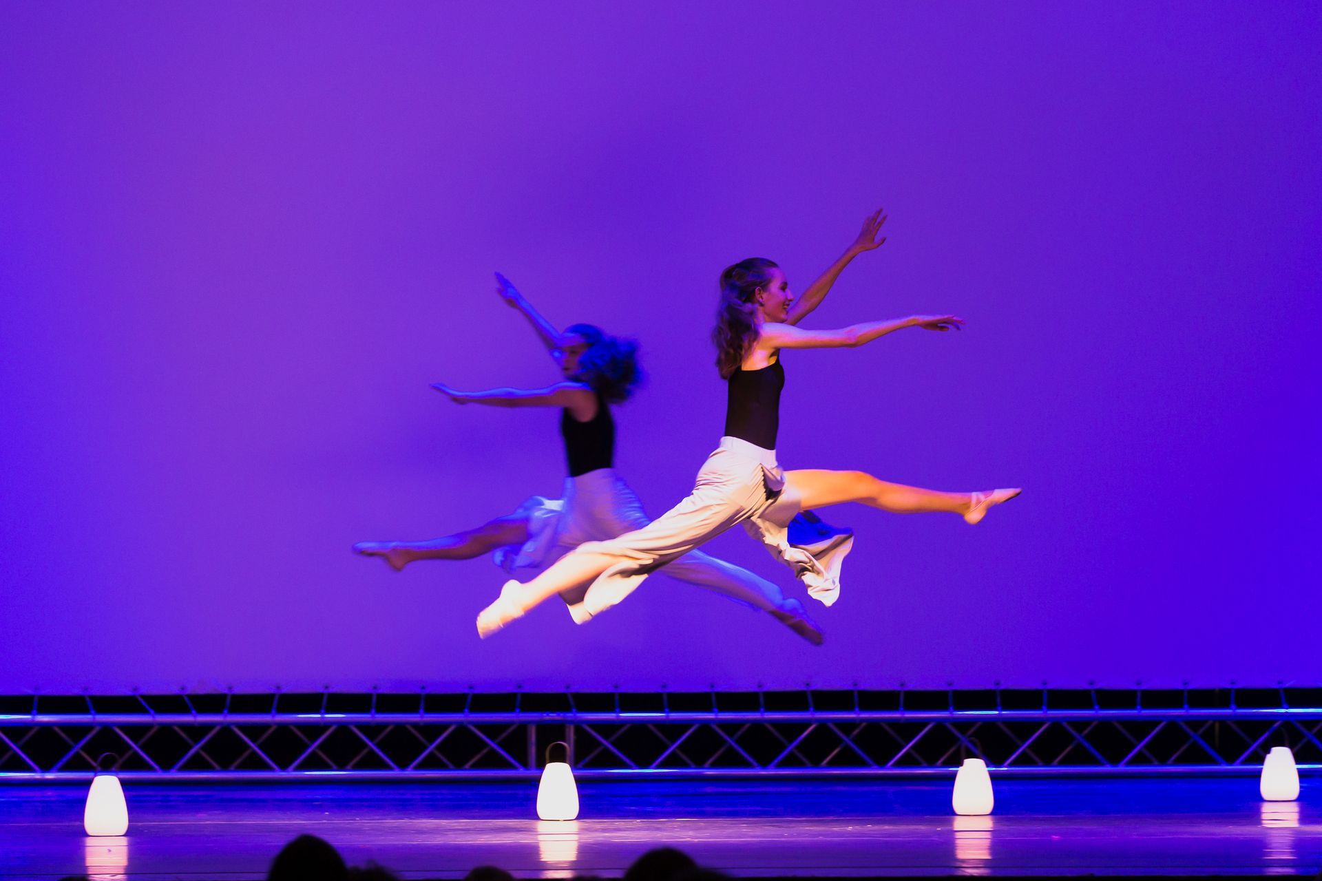 Zwei Tänzer springen auf einer Bühne in die Luft.