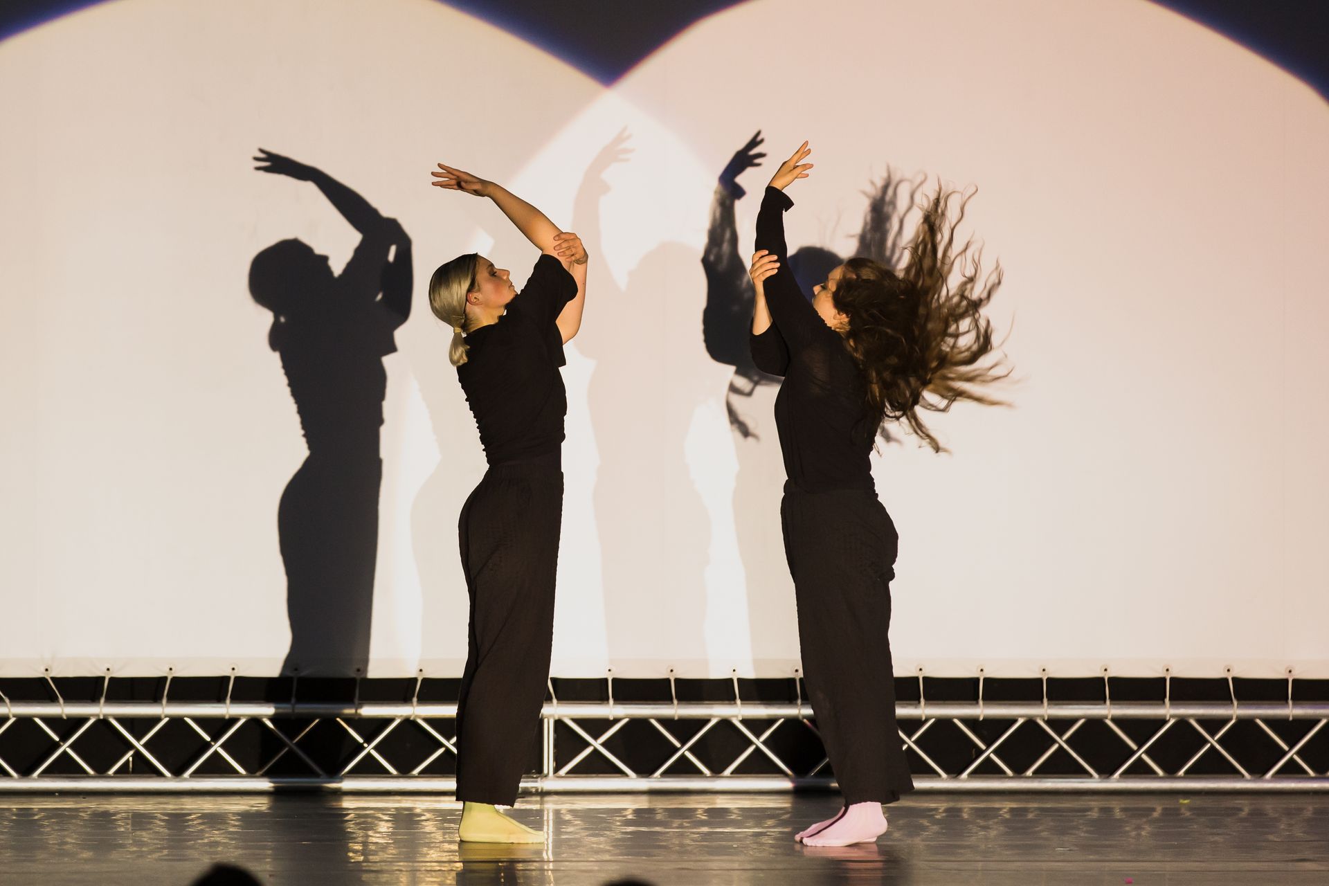 Drei Frauen tanzen auf einer Bühne und ihre Schatten werden auf die Wand hinter ihnen projiziert.