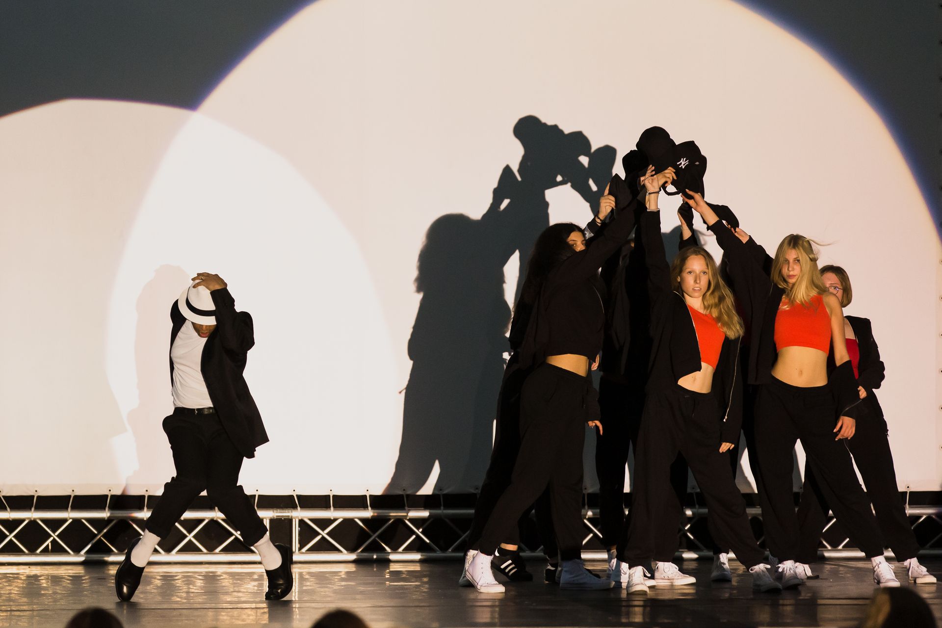 Eine Gruppe von Menschen tanzt auf einer Bühne vor einer Projektionsleinwand.