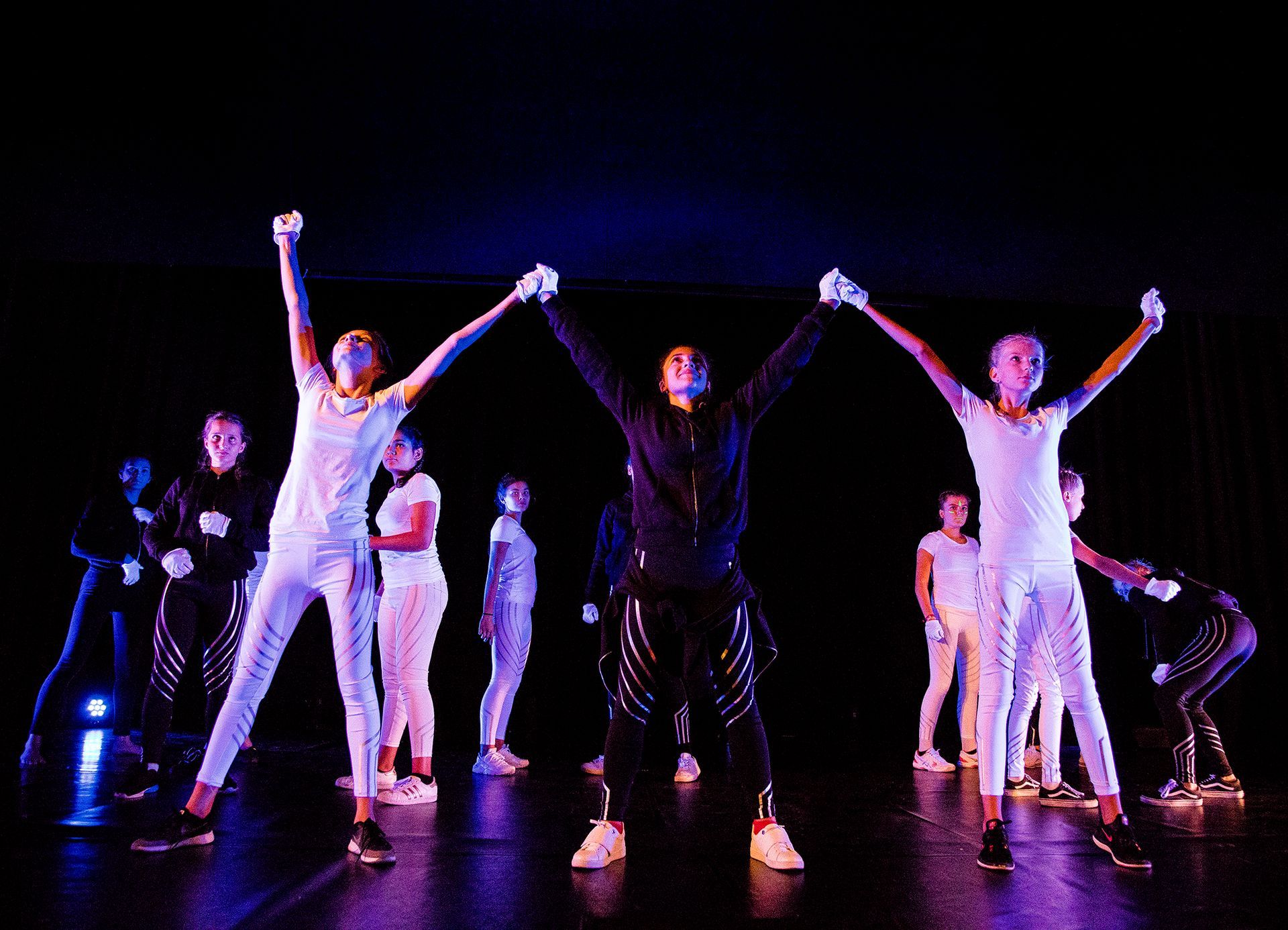 Eine Gruppe junger Leute tanzt mit erhobenen Armen auf einer Bühne.