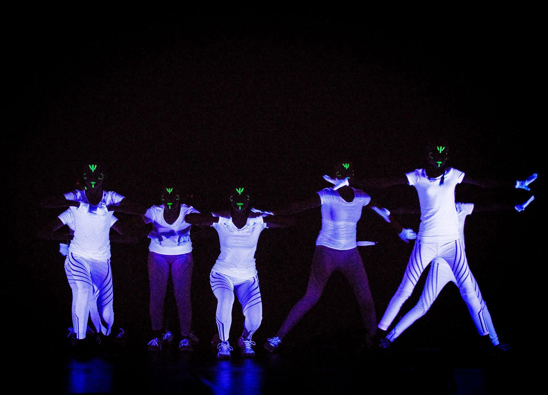Eine Gruppe von Menschen tanzt in einem dunklen Raum mit im Dunkeln leuchtender Kleidung.