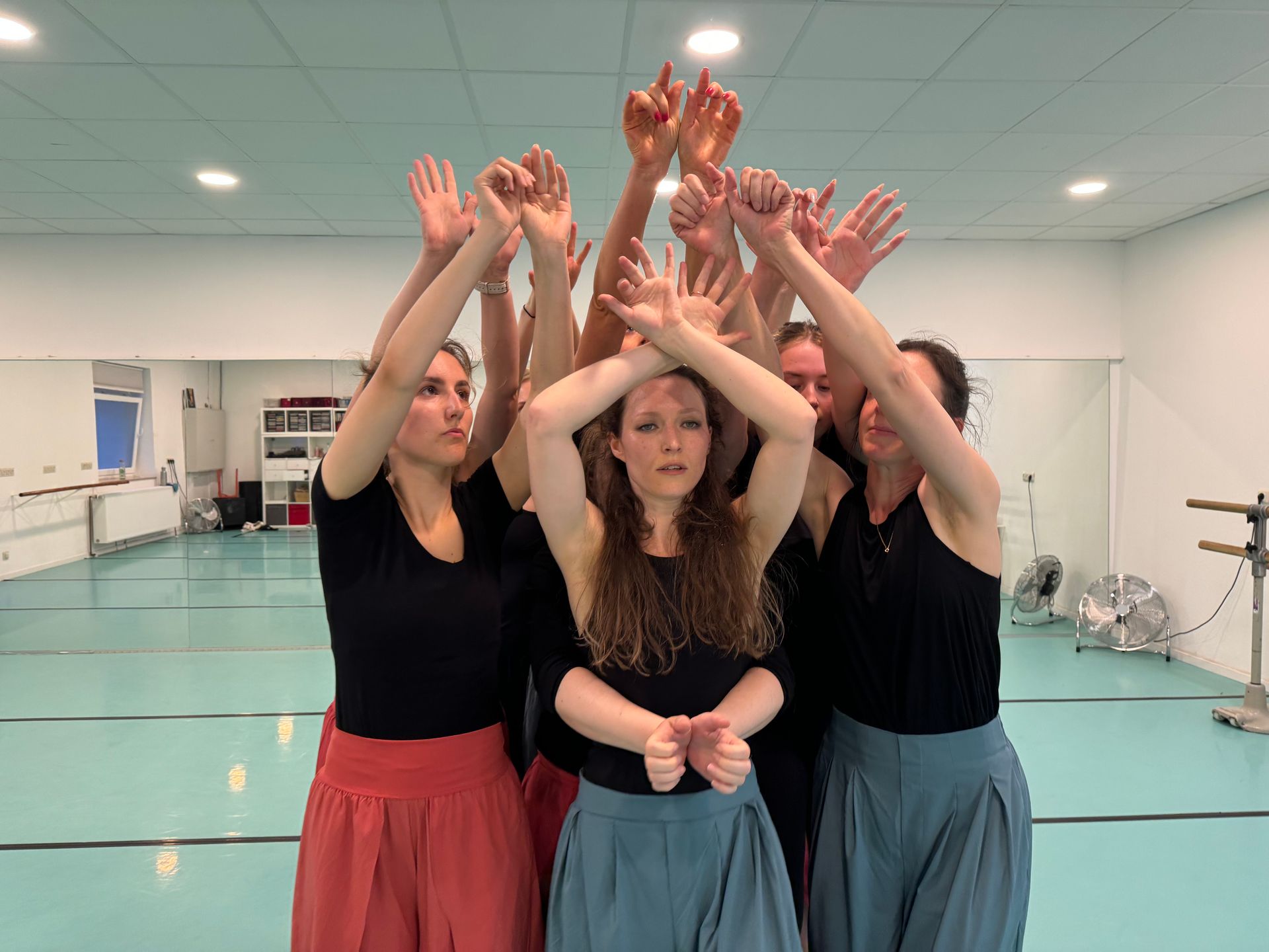 Eine Gruppe von Frauen steht mit erhobenen Händen in einem Tanzstudio.