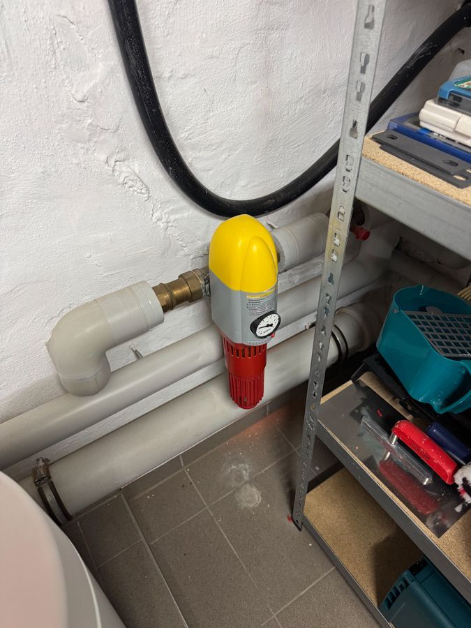 Ein gelb-rotes Gerät ist an einem Rohr in einem Badezimmer befestigt.