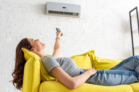 Une jeune femme règle sa climatisation avec une télécommande