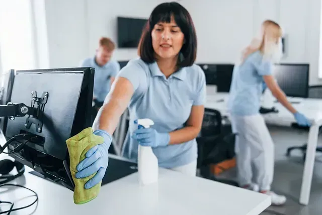 Una mujer está limpiando un monitor de computadora con un paño en una oficina.