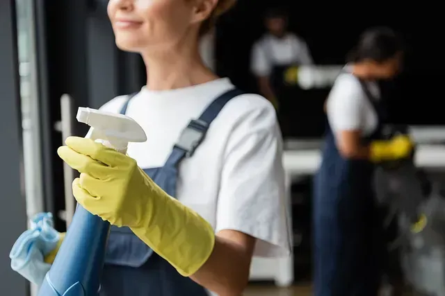Una mujer con guantes amarillos sostiene una botella de spray y un trapeador.