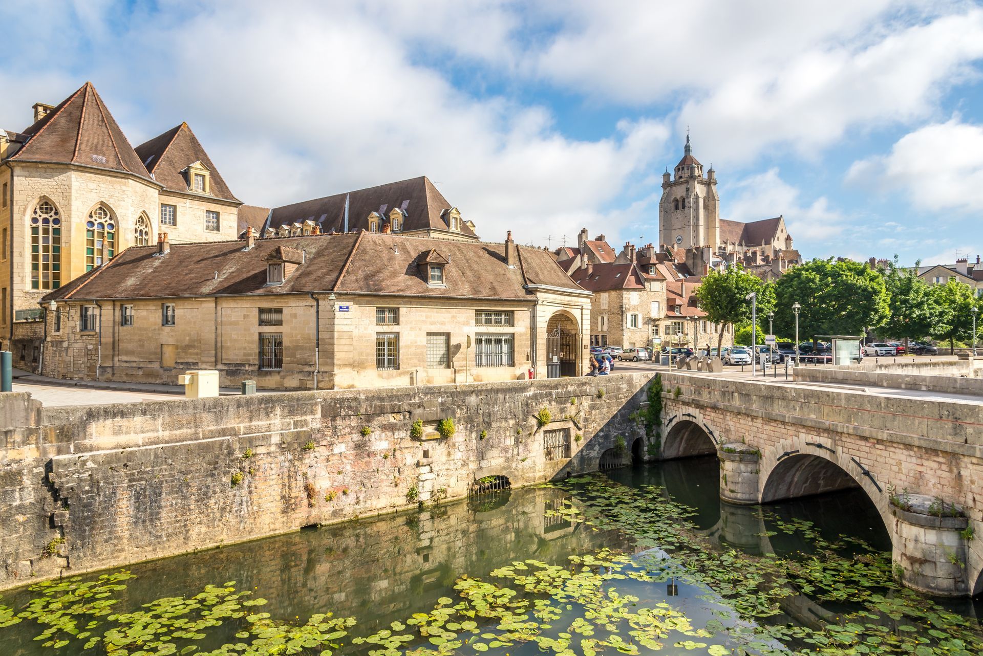 Une ville historique en pierre, traversée par un pont enjambant un canal, avec ses bâtiments traditionnels aux toits de tuiles.