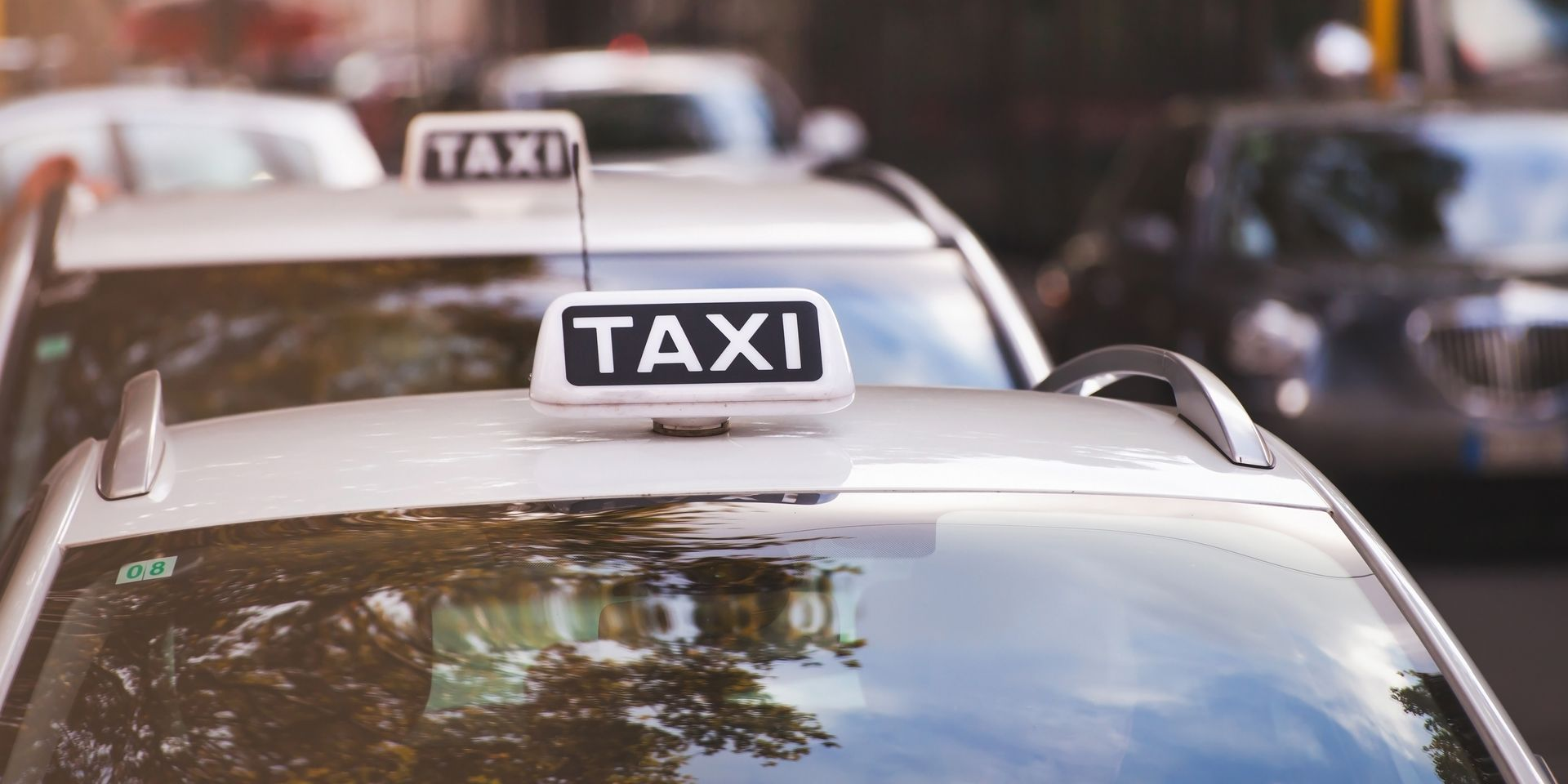 Plusieurs taxis sont alignés dans une rue de la ville, leurs panneaux de taxi sur le toit étant particulièrement visibles.
