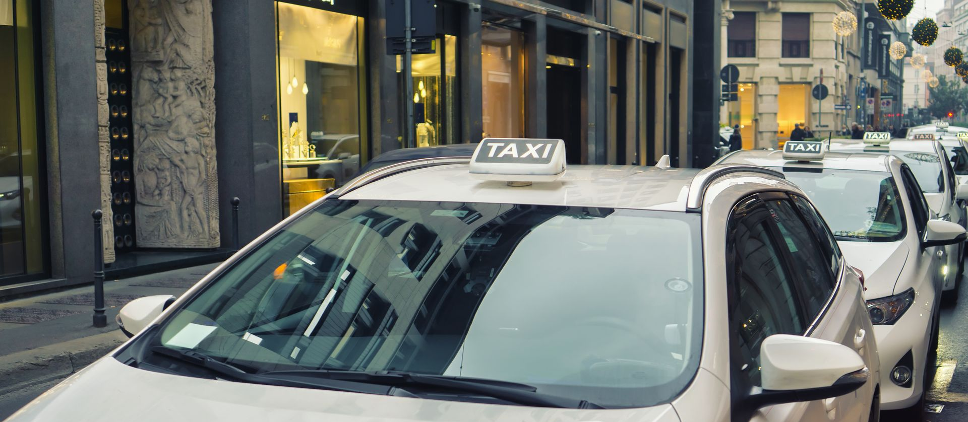 Une file de taxis stationnés dans une rue de la ville, devant les devantures des magasins.
