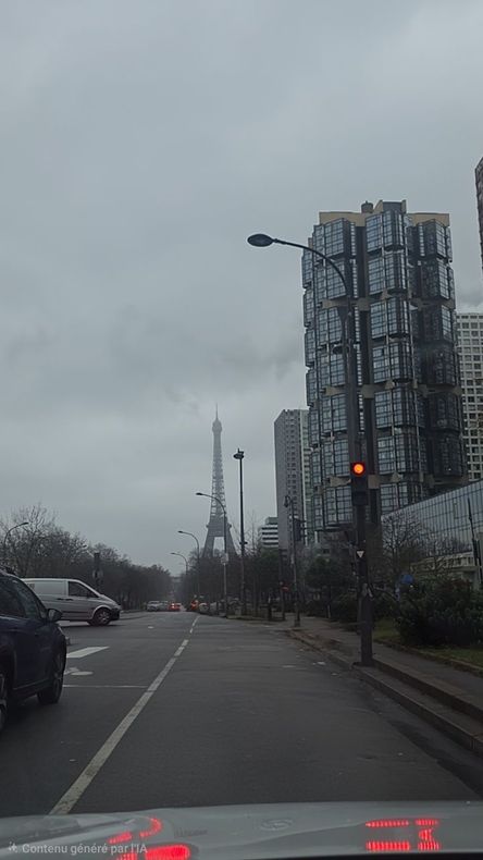 La tour Eiffel se dresse au loin par une journée nuageuse, vue depuis une rue de la ville, à côté d'une tour de verre moderne.