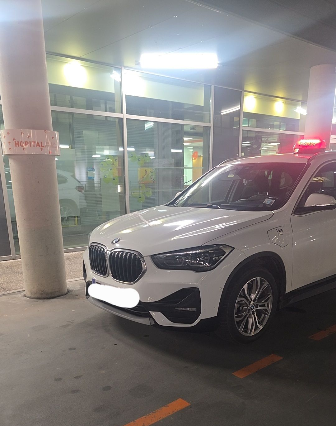 Un SUV BMW garé à l'intérieur, sous un plafonnier lumineux, près d'un pilier en béton.