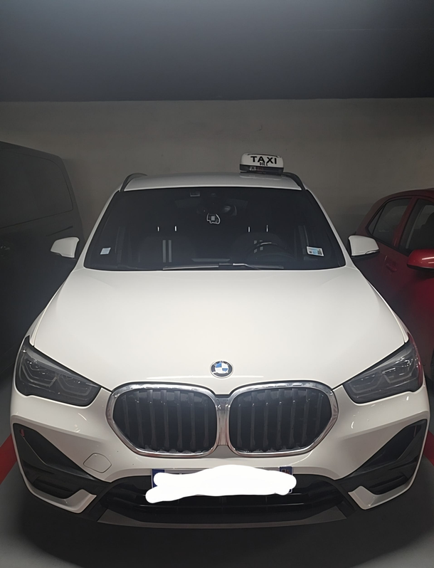 Un SUV BMW X1 garé dans un garage, face à la route, avec un panneau de taxi sur le toit.