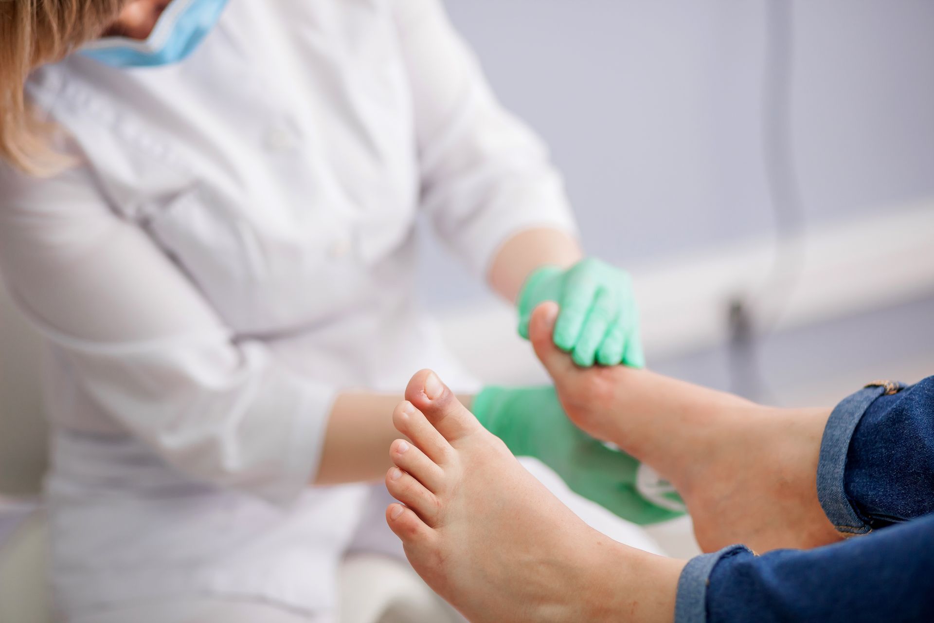 Ärztin untersucht den Fuss einer Patientin. Sie trägt einen Laborkittel, Handschuhe und eine Maske.