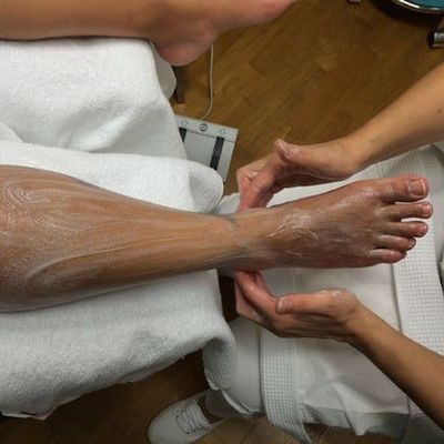 In einer Spa-ähnlichen Umgebung werden Bein und Fuss einer Person von den Händen einer anderen Person massiert.