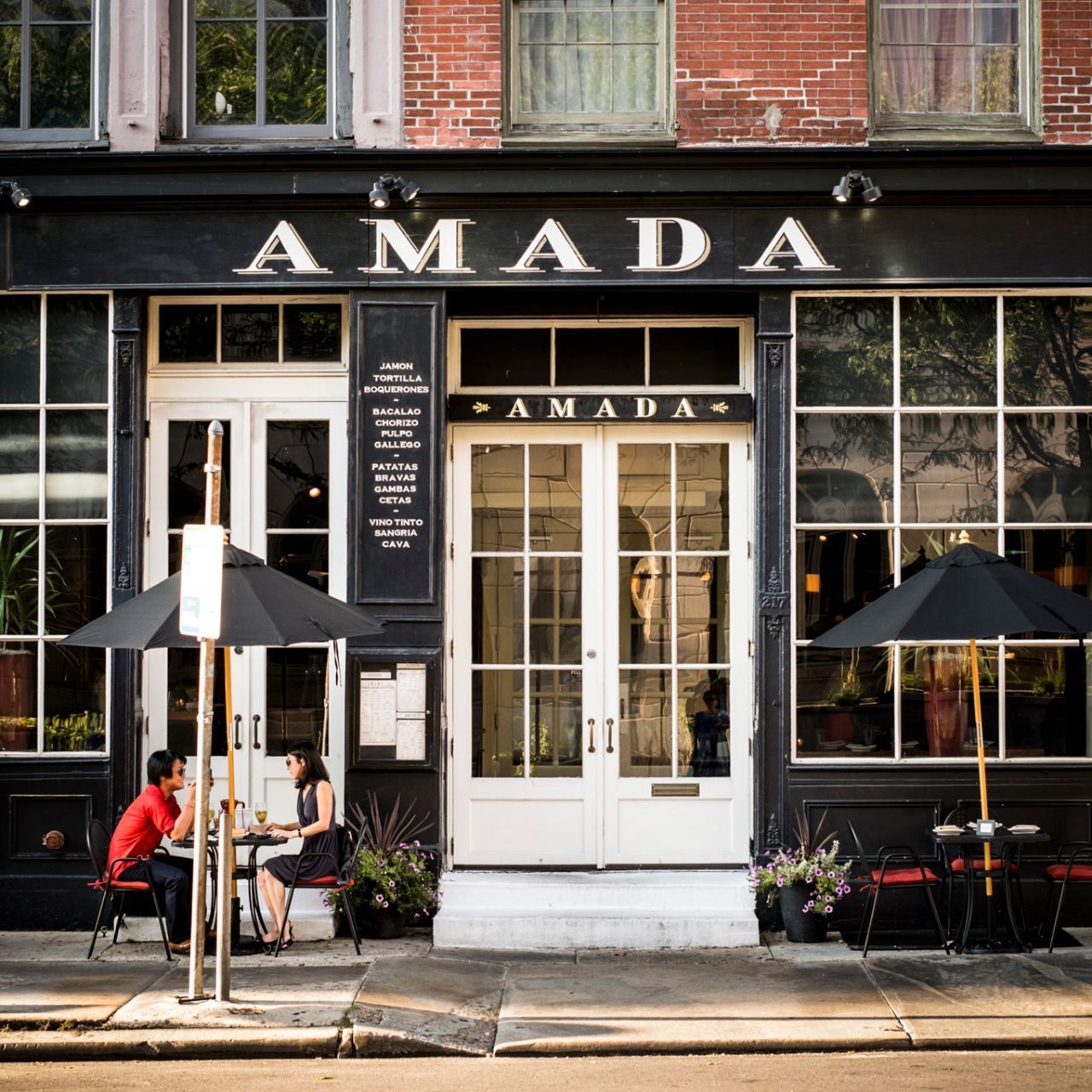 Two people sit at tables outside of the amada restaurant