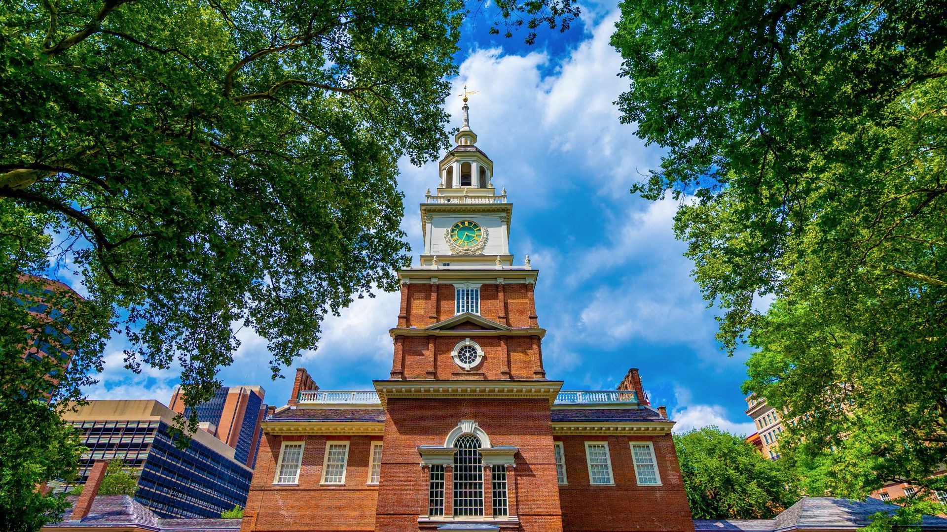 A large brick building with a clock tower is surrounded by trees on a sunny day.