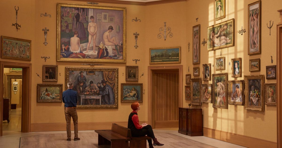A woman is sitting on a bench in a museum looking at paintings.