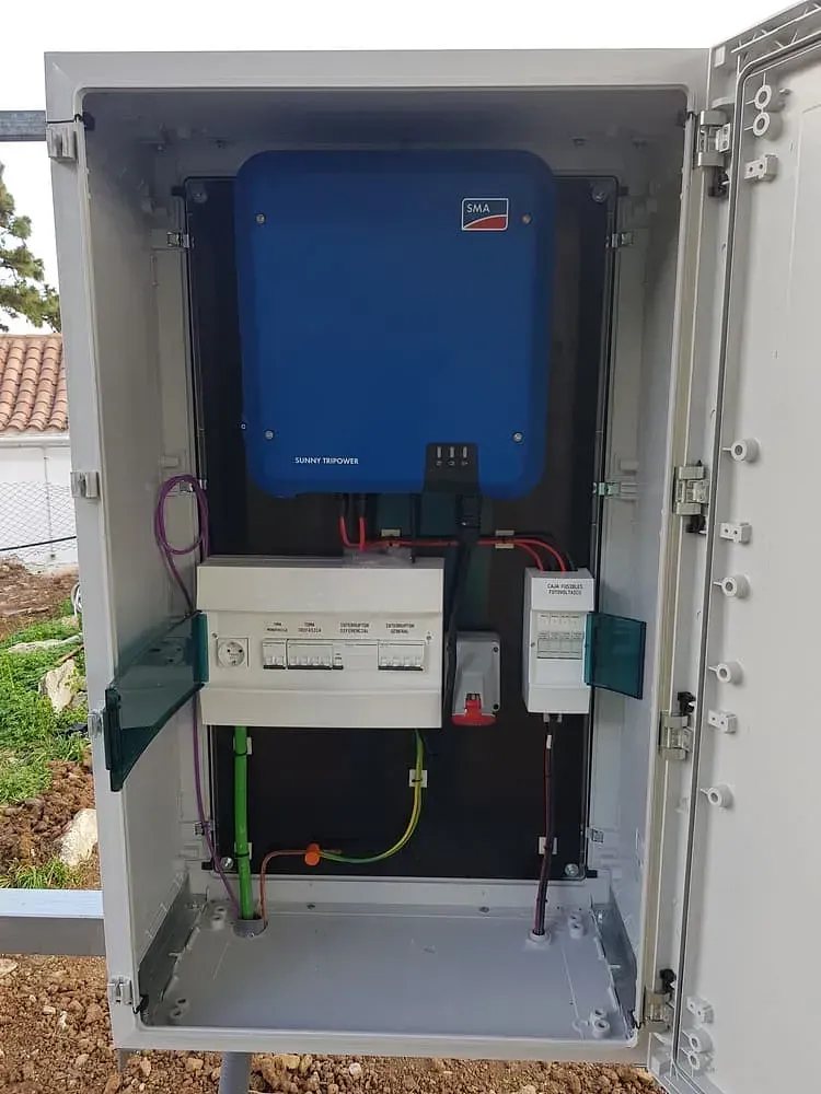 Caja metálica abierta que alberga los componentes del panel solar, incluido un inversor azul, un panel eléctrico con interruptores y cableado.