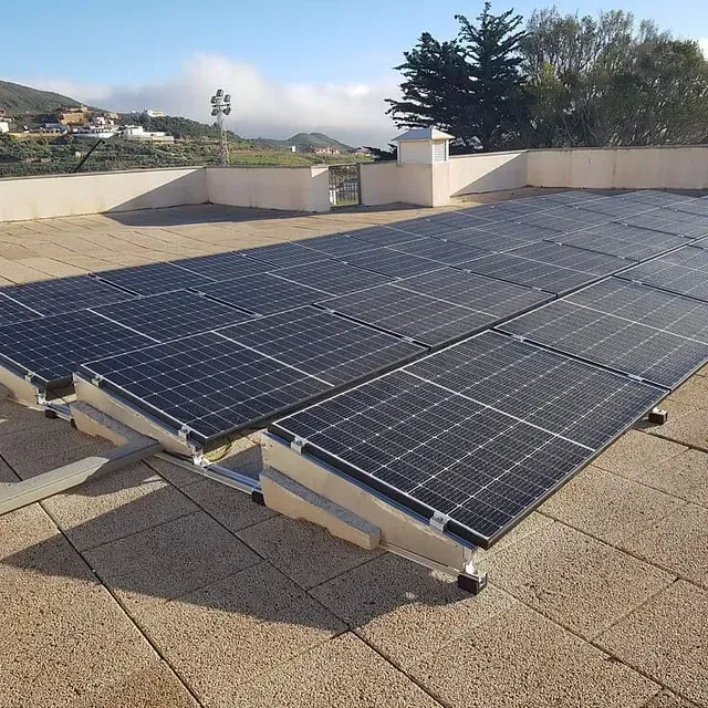 Paneles solares instalados en un tejado plano con vistas a una ciudad al fondo bajo un cielo azul.