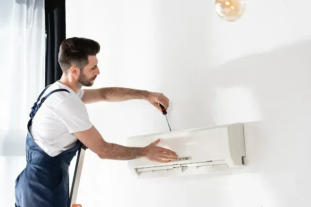Un hombre con mono instala una unidad de aire acondicionado montada en la pared sobre una pared blanca.