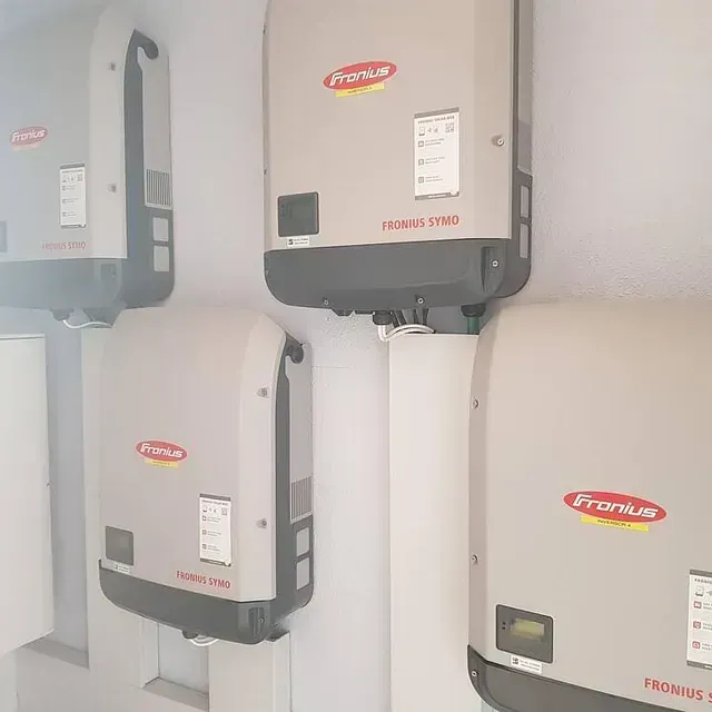 Varios inversores solares Fronius grises montados en una pared blanca. Los inversores lucen el logotipo de la empresa en rojo y amarillo.