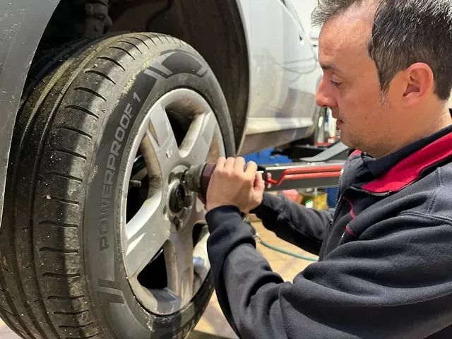 Un hombre está cambiando un neumático de un coche con una llave inglesa.